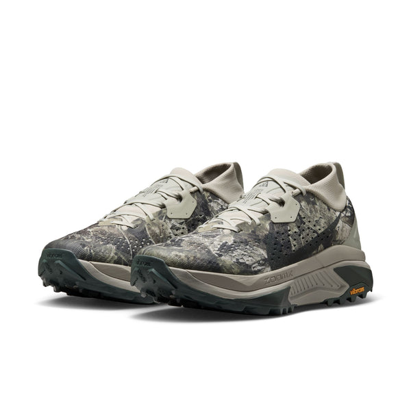 Et par Nike ACG Zegama trail-løbesko til mænd i farvekombinationen Spruce Fog/Black Spruce-Sea Glass-Black, med et gråt og grønt camouflage-inspireret design, tykke såler med struktureret mønster, lysegrå snørebånd og en Vibram Megagrip-ydersål for forbedret greb – en kombination af holdbarhed og ydeevne inspireret af den klassiske Nike ACG Zegama.
