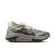 En enkelt Nike ACG Zegama-løbesko til mænd i farvekombinationen Spruce Fog/Black Spruce-Sea Glass-Black, med en grå og beige overdel i camouflagemønster, hvide snørebånd og en tyk sål i mørke og lyse nuancer med Vibram Megagrip-teknologi. Det gule Vibram-logo er placeret tæt på hælen. Skoen, der er inspireret af trail-løbesko og designet til kuperet terræn, vises her i et sidebillede.