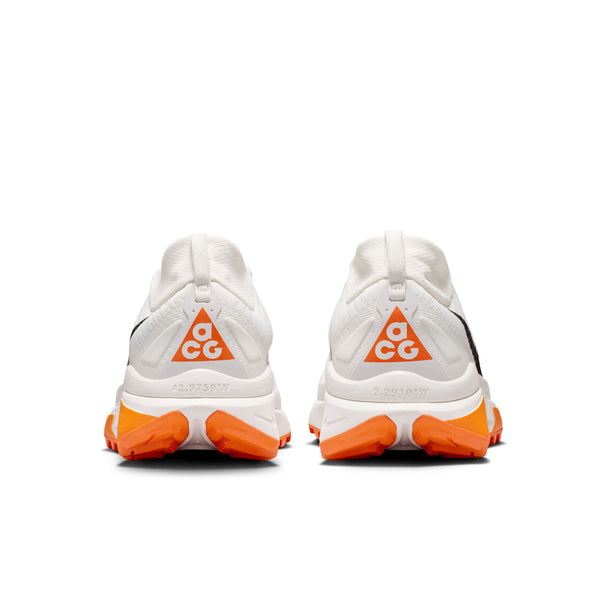 Et par Nike ACG Zegama Dame trailsko i Summit White/Black-Phantom-Safety Orange, vist bagfra med orange og hvide trekantede ACG-hæl-logoer, orange såldetaljer og koordinater trykt på mellemsålerne.