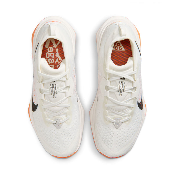 Topbillede af Nike ACG Zegama Dame trailsko i Summit White/Black-Phantom-Safety Orange med orange indlægssåler med hvidt branding, sorte swooshes på siden, orange Vibram Megagrip-såler, hvide snørebånd og overdel i mesh.