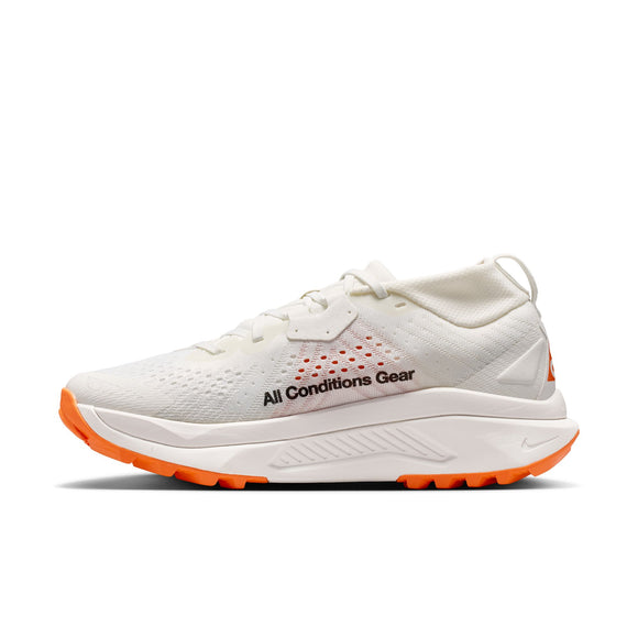 Nike ACG Zegama Dame i Summit White/Black-Phantom-Safety Orange har en overdel i mesh, orange detaljer på sålen og hælen, All Conditions Gear-branding, snørelukning, lav profil og en Vibram Megagrip-ydersål med godt greb.