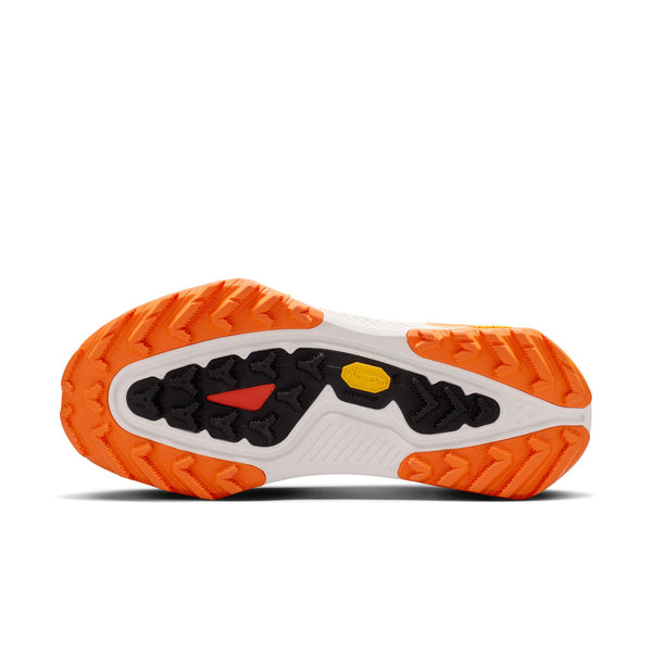 Billedet viser sålen på Nike ACG Zegama Dame trailsko i Summit White/Black-Phantom-Safety Orange med en orange og sort slidbane og et gult Vibram Megagrip-logo på en hvid baggrund.