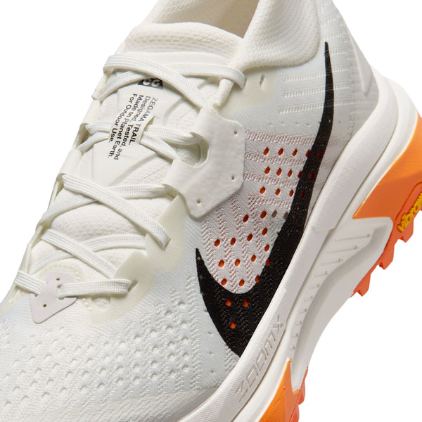 Et nærbillede af Nike ACG Zegama Dame i Summit White/Black-Phantom-Safety Orange fremhæver en sort swoosh, orange Vibram Megagrip-sål, hvide snørebånd, mesh-detaljer og logotekst på tungen.