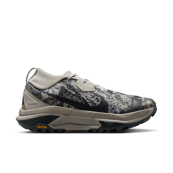 En Nike ACG Zegama trail-løbesko til kvinder i farvekombinationen Spruce Fog/Black Spruce-Sea Glass-Black, med en mønstret overdel i grå og sorte nuancer, en tyk sål, Vibram-logo på ydersålen med Vibram Megagrip-teknologi samt teksten »Zegama« på siden. Skoen vises i profil mod en hvid baggrund.