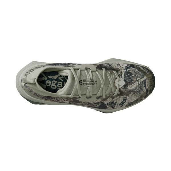 Her er en omskrevet sætning, der bruger dine produktdata: Set ovenfra viser Nike Acg Zegama til kvinder i farvekombinationen Spruce Fog/Black Spruce-Sea Glass-Black et grønt og brunt camouflagemønster, lysegrå snørebånd og indlægssål med mærkelogo. Denne sko, der minder om innovative trail-løbesko-designs, har en tyk sål med Vibram Megagrip, der sikrer bedre greb og et moderne look.