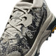 Et nærbillede af Nike ACG Zegama Dame-trail-løbeskoen viser den camouflagemønstrede overdel i farven Spruce Fog med grå snørebånd og en mørkegrå sål. Skoen har et synligt mærke på tungen og Vibram Megagrip-logoet på sålen tæt på hælen, hvilket understreger det præstationsinspirerede design i farvekombinationen Black Spruce-Sea Glass-Black.