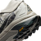 Nærbillede af hælen og sålen på en lys trail-løbesko, nærmere bestemt Nike Acg Zegama Dame i farvekombinationen Spruce Fog/Black Spruce-Sea Glass-Black, der viser et Vibram Megagrip-logo på det sorte slidbane og et delvist billede af skoens overdel med dens strukturerede designelementer.