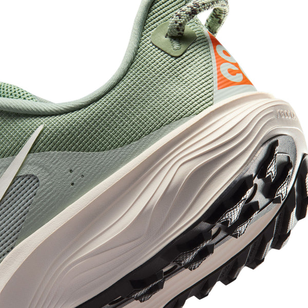 Nærbillede af hælen på en Nike ACG Pegasus Trail Dame i Jade Horizon/Phantom-Light Silver, der viser struktureret stof, en løkke bagpå, orange mærkevaredetaljer og en robust sort og hvid sål med dybe slidbaner.