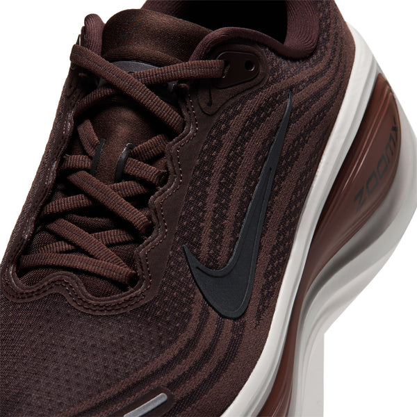 Nærbillede af en Nike Vomero Plus, Herre, Baroque Brown/Black-Phantom løbesko i brun, med et sort Swoosh-logo på siden og en tyk hvid og brun mellemsål.