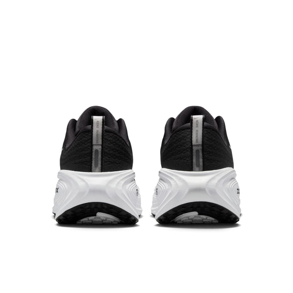 Et par Nike Vomero Plus-løbesko til kvinder i farvekombinationen Black/White-Cool Grey-Mtlc Dark Grey set bagfra, med struktureret overdel, tykke hvide såler, der sikrer maksimal komfort, og en reflekterende stribe på hver hæl. Baggrunden er ensfarvet hvid.