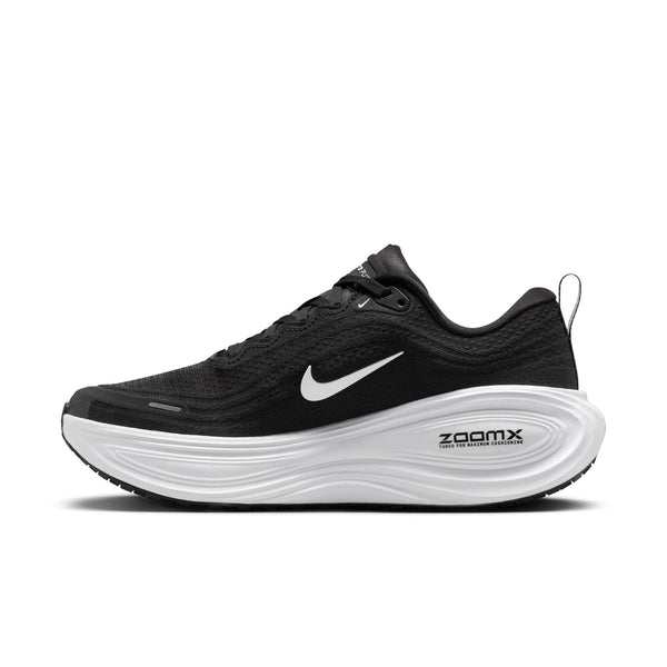 En Nike Vomero Plus-løbesko til kvinder i farven Black/White-Cool Grey-Mtlc Dark Grey, med et hvidt Nike-swoosh-logo, sorte snørebånd og en hvid ZoomX-sål, der sikrer maksimal komfort, fotograferet fra siden mod en hvid baggrund.