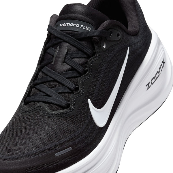 Et nærbillede af Nike Vomero Plus Dame-løbeskoen i farvekombinationen Sort/Hvid-Cool Grey-Mtlc Mørkegrå, der fremhæver det hvide Swoosh-logo og »Vomero Plus«-mærket på tungen. Den sorte overdel i mesh, de sorte snørebånd og ZoomX-logoet på den hvide sål understreger alle sammen designet, der er skabt til maksimal komfort under hver eneste løbetur.