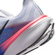 Nærbillede af hælen på en Nike Pegasus 42 Herre-løbesko i farvekombinationen Hvid/Sort-Racerblå-Atomic Pink, der viser den hvide og blå mesh-overdel med en accentstribe i Atomic Pink. Den strukturerede hvide ydersål har et sort mønster, mens ReactX-skum-mellemsålen og Air Zoom-teknologien er sømløst integreret for øget komfort og ydeevne.