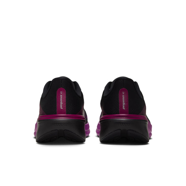 Et par Nike Pegasus 42 Dame-sportssko i farvekombinationen SORT/METALLISK SØLV-LIVLIG LILLA vises set bagfra, hvilket fremhæver de livlige lilla detaljer på sålerne og hælflapperne. Designet er udstyret med den avancerede ReactX-skum-mellemsål, der sikrer enestående komfort, alt sammen mod en ensfarvet hvid baggrund.