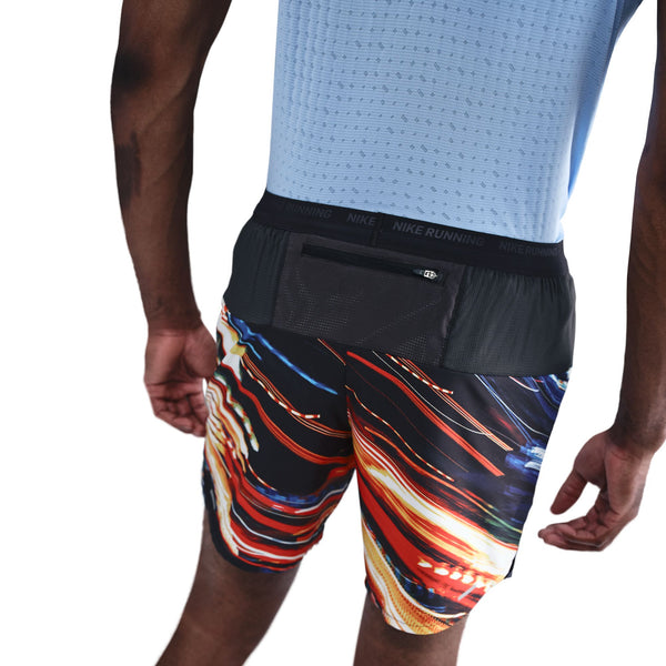 En person iført en lyseblå sportstrøje og Nike Nk Df Stride 7In Bf Shrt Op2 herreshorts i hvid/multifarvet/reflekterende sølv, med en lille lynlåslomme bag på linningen, set bagfra.