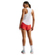 En person står med ryggen til og er iført en hvid/sort Nike AeroSwift Running Singlet (Dame), røde shorts, hvide strømper midt på læggen og hvide sneakers med grønne og pink detaljer. Vedkommende har også solbriller og tilbagestrøget hår.