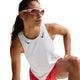 En person iført en hvid/sort Nike AeroSwift Running Singlet til kvinder poserer med et løftet knæ, sammen med røde shorts og reflekterende sportssolbriller mod en hvid baggrund.