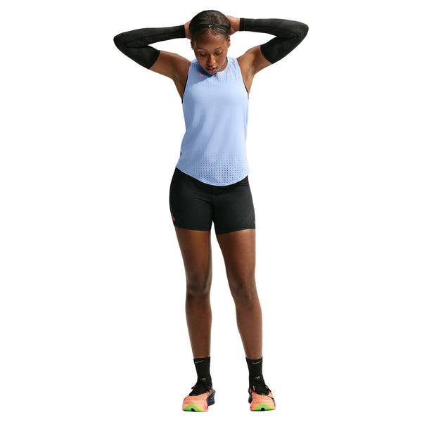 En person iført en Nike AeroSwift løbetrøje (Dame), farven Aluminium/Atomic Pink, sorte shorts, armvarmere, strømper og flerfarvede løbesko står med hænderne foldet bag hovedet og kigger ned.