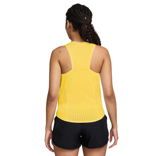 En kvinde med flettet hår ses bagfra iført en Nike AeroSwift Running Singlet for women i Citron Pulse/Black og sorte shorts, stående mod en almindelig hvid baggrund.