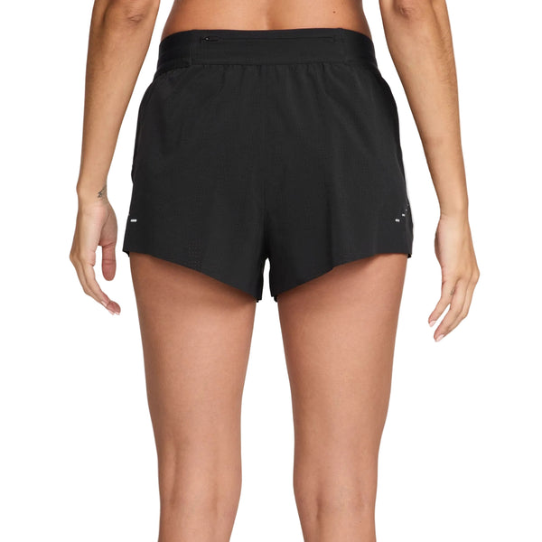 En kvinde ses bagfra iført Nike Swift Breathe Mid-Rise 2.5" løbeshorts i sort/sort/hvid/reflekterende sølv, stående med armene afslappet i siden mod en almindelig hvid baggrund.