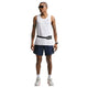 En mand med solbriller og en hvid ærmeløs top bærer Nike Stride 2In1 7" løbeshorts til mænd i Midnight Navy/Reflective Silver, plus hvide sokker, sportssko, tatoveringer, et smartur og et sort taljebælte på en hvid baggrund.