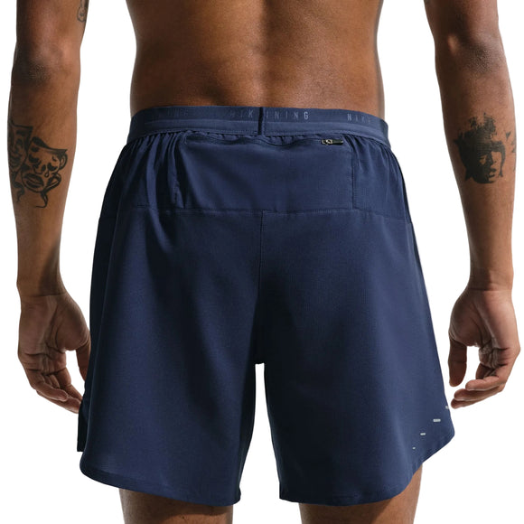 En person i bar overkrop med tatoveringer på begge arme ses bagfra iført Nike Stride 2In1 7" løbeshorts til mænd i Midnight Navy/Reflective Silver med elastisk linning.