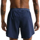 En person i bar overkrop med tatoveringer på begge arme ses bagfra iført Nike Stride 2In1 7" løbeshorts til mænd i Midnight Navy/Reflective Silver med elastisk linning.