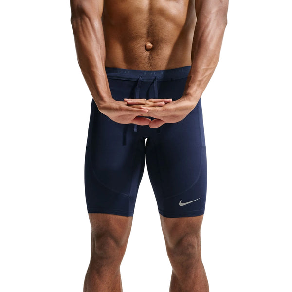En mand, der står med armene bag ryggen og fingrene flettede, viser Nike Stride Running Half Tights til mænd i farven Midnight Navy/Reflective Silver. Billedet, der er beskåret fra brystet til knæene på en hvid baggrund, fremhæver det svedtransporterende løbetøj – perfekte løbetights til mænd, der er designet til atleter, der prioriterer komfort og ydeevne.