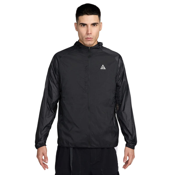 En mand med kort mørkt hår og et neutralt udtryk ser frem for sig iført Nike ACG Uv Aireez Jkt Herre i Black/Black/Summit White med et lille hvidt trekantslogo på venstre bryst og teksturerede ærmer.