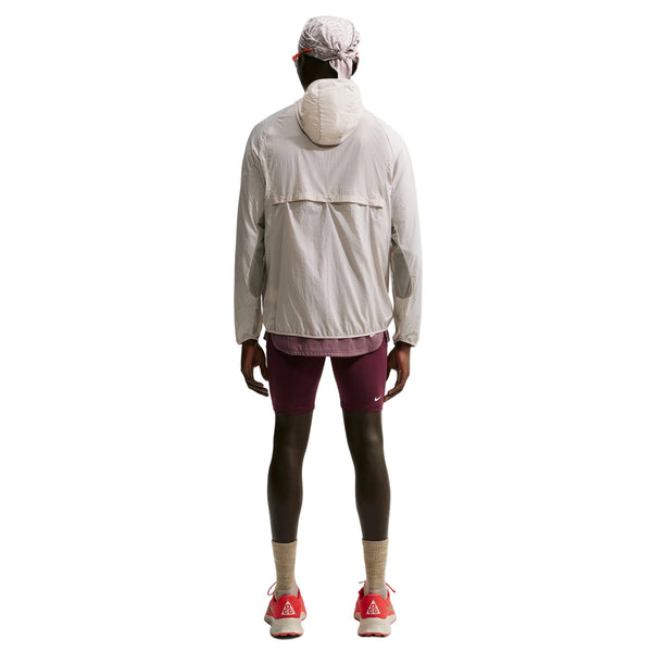 En person set bagfra, iført en Nike ACG Aireez UV Protection Jacket, Herre, Cream II /Cream II /Summit White, mørke shorts og røde sportssko.