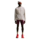 En mand iført en Nike ACG Aireez UV Protection Jacket, Herre, Cream II /Cream II /Summit White, rødbrune sportsshorts, røde solbriller og røde løbesko.