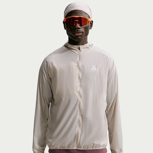 En person iført en Nike ACG Aireez UV Protection-jakke, Herre, farven Cream II / Cream II / Summit White, orange reflekterende solbriller og et mønstret tørklæde.