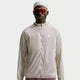 En person iført en Nike ACG Aireez UV Protection-jakke, Herre, farven Cream II / Cream II / Summit White, orange reflekterende solbriller og et mønstret tørklæde.