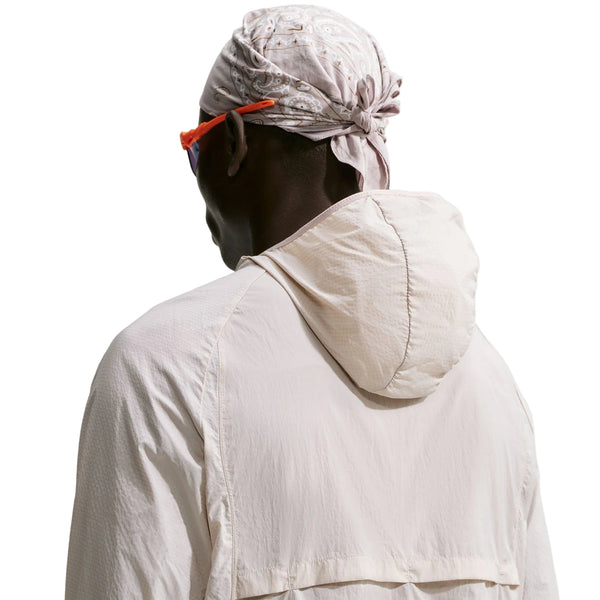 Bagfra-billede af en person iført en Nike ACG Aireez UV Protection Jacket, Herre, Cream II / Cream II / Summit White, solbriller og et mønstret hovedtørklæde.