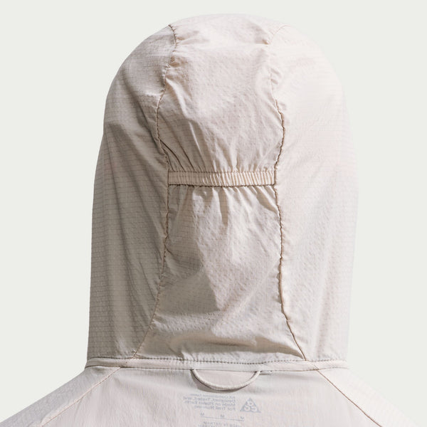 Bagfra set billede af en cremefarvet Nike ACG Aireez UV Protection-jakke med stof i gittermønster og en justerbar snor i hætten.