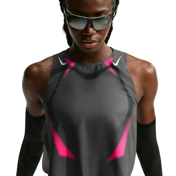 En person iført mørke solbriller, sorte armvarmere og Nike AeroSwift Cropped Running Tank Top til kvinder i farvekombinationen Iron Grey/Volt/White (ærmeløs Dri-FIT ADV), fotograferet fra livet og opefter på en hvid baggrund.