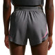 Der vises en person fra livet og ned, iført Nike AeroSwift 3In Shorts Gx til kvinder i farven Iron Grey/White. Disse løbeshorts er udstyret med Dri-FIT ADV-teknologi, der sikrer optimal komfort og ydeevne. Baggrunden er ensfarvet og neutral.