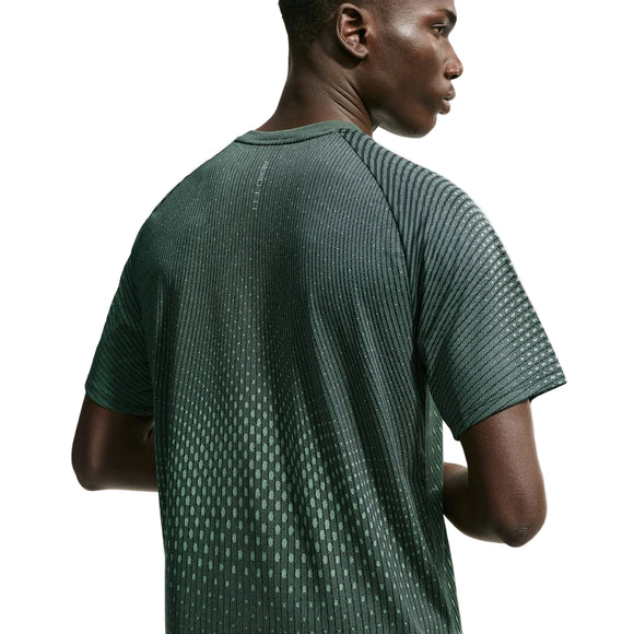 Der ses et billede af en mand set bagfra, iført Nike Stride Aero-FIT kortærmet løbetrøje i farvekombinationen sort/lysegrøn Spark/reflekterende sølv. Denne herre-løbetrøje er designet til optimal ventilation og har et struktureret, prikket mønster, der træder tydeligt frem mod den ensfarvede hvide baggrund.