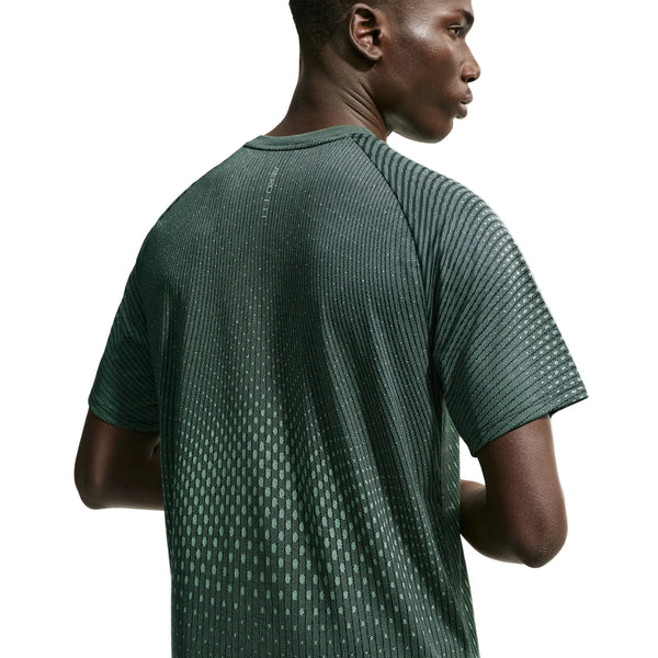 Der ses et billede af en mand set bagfra, iført Nike Stride Aero-FIT kortærmet løbetrøje i farvekombinationen sort/lysegrøn Spark/reflekterende sølv. Denne herre-løbetrøje er designet til optimal ventilation og har et struktureret, prikket mønster, der træder tydeligt frem mod den ensfarvede hvide baggrund.