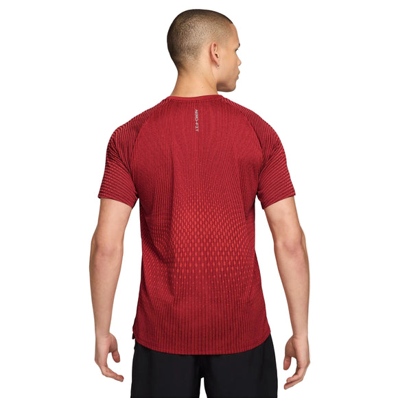 Man ser en person set bagfra, der bærer en Nike Stride Aero-FIT kortærmet løbetrøje til mænd i farverne Tough Red/Bright Crimson/Reflective Silver, kombineret med sorte shorts. Denne sportstrøje har et diskret farveforløb og et lille reflekterende sølvlogo tæt på halsen. Den åndbare træningstrøje giver øget komfort, mens personens korte hår fuldender det atletiske look.