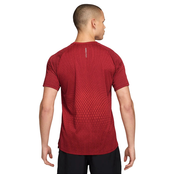 Man ser en person set bagfra, der bærer en Nike Stride Aero-FIT kortærmet løbetrøje til mænd i farverne Tough Red/Bright Crimson/Reflective Silver, kombineret med sorte shorts. Denne sportstrøje har et diskret farveforløb og et lille reflekterende sølvlogo tæt på halsen. Den åndbare træningstrøje giver øget komfort, mens personens korte hår fuldender det atletiske look.