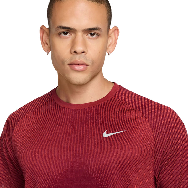 En person med kort hår og hoop-øreringe i begge ører ser direkte ind i kameraet, iført Nike Stride Aero-FIT kortærmet løbetrøje til mænd i farverne Tough Red/Bright Crimson/Reflective Silver. Den åndbare træningstrøje har en struktureret overflade med et lille, reflekterende sølvfarvet Nike-logo på venstre bryst, hvilket sikrer optimal ydeevne og komfort – ideel som løbetrøje til mænd.