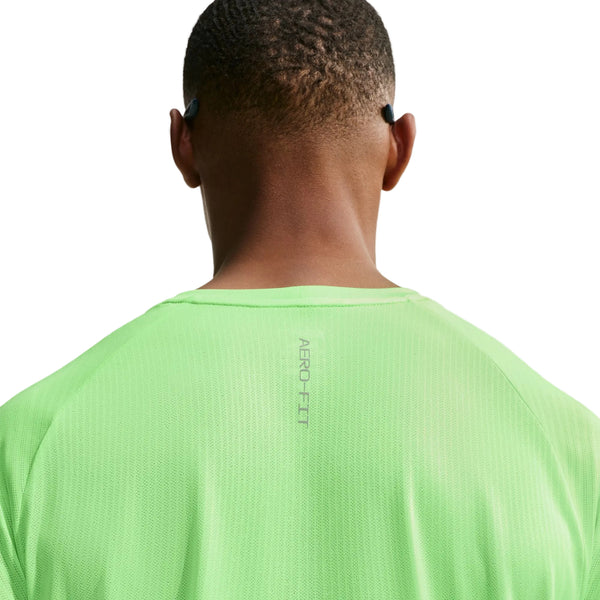 Der vises en person set bagfra, iført en lys voltgrøn Nike Stride Aero-FIT kortærmet løbetrøje til mænd med detaljer i lys sølv og reflekterende sølv. Toppen har teksten »AERO.FIT« trykt øverst på ryggen og er designet til maksimal ventilation. Personen har kortklippet hår og sorte øretelefoner, med en ensfarvet hvid baggrund.