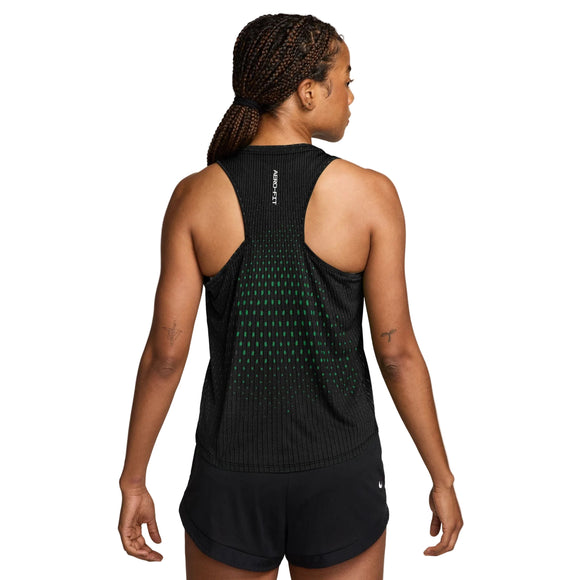 En kvinde med flettet hår ses bagfra, iført Nike Swift Aero-FIT løbetop til kvinder i farvekombinationen sort/lysegrøn Spark/reflekterende sølv samt matchende sorte shorts. Den ærmeløse sportstop er designet til maksimal ventilation og er prydet med små grønne prikker samt teksten »AEROREADY« trykt tæt på kraven. Hun står foran en ensfarvet hvid baggrund.