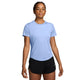 En person står med ansigtet vendt fremad og er iført en lyseblå Nike Swift Aero-FIT kortærmet løbetrøje til kvinder i farverne Aluminium/Pure Platinum/Reflective Silver samt sorte Nike-shorts. Baggrunden er ensfarvet hvid, og personen har et neutralt udtryk, mens armene hænger afslappet ned langs siden. Den ventilerende løbetrøje sikrer maksimal komfort under enhver løbetur.
