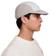 En person i profil vender mod højre og er iført en Nike ACG Fly Cap (unisex, Photon Dust/College Grey/Photon Dust) og en råhvid skjorte. Vedkommende har kort mørkt hår og en lille ørering i venstre øre.