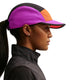 En person i profil bærer en Nike ACG Fly Cap Unisex i Safety Orange/Vivid Purple/Safety Orange og en sort jakke. Vedkommende har hestehale, små ørestikker og står på en hvid baggrund.