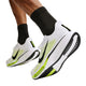 Der vises en person, der går eller løber, med fokus på underbenene og Nike Pegasus Plus 2, Herre-skoene i farvekombinationen HVID/SORT-LEMON VENOM, som har sorte Nike-swooshes og responsiv ZoomX-skum-støddæmpning, set på en ensfarvet hvid baggrund.