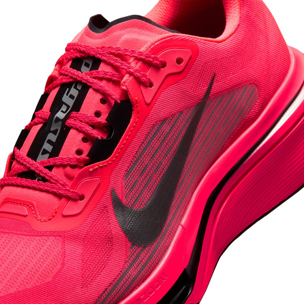 Nærbillede af en lys „Flash Crimson“-farvet Nike Pegasus Plus 2 herresko med detaljer i sort og metallisk sølv, hvor det markante Nike Swoosh-logo træder tydeligt frem. Overdelen i mesh, de strukturerede snørebånd og den synlige Zoom-støddæmpning på sålen er iøjnefaldende. Denne løbesko er vinklet, så man kan se den fra siden og delvist ovenfra, hvilket fremhæver den avancerede ZoomX-skum, der sikrer responsiv komfort under hver eneste løbetur.