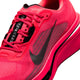 Nærbillede af en lys „Flash Crimson“-farvet Nike Pegasus Plus 2 herresko med detaljer i sort og metallisk sølv, hvor det markante Nike Swoosh-logo træder tydeligt frem. Overdelen i mesh, de strukturerede snørebånd og den synlige Zoom-støddæmpning på sålen er iøjnefaldende. Denne løbesko er vinklet, så man kan se den fra siden og delvist ovenfra, hvilket fremhæver den avancerede ZoomX-skum, der sikrer responsiv komfort under hver eneste løbetur.